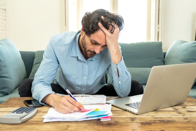 young angry and worried man working with laptop at home looking at bills and paying bills in home finance concept